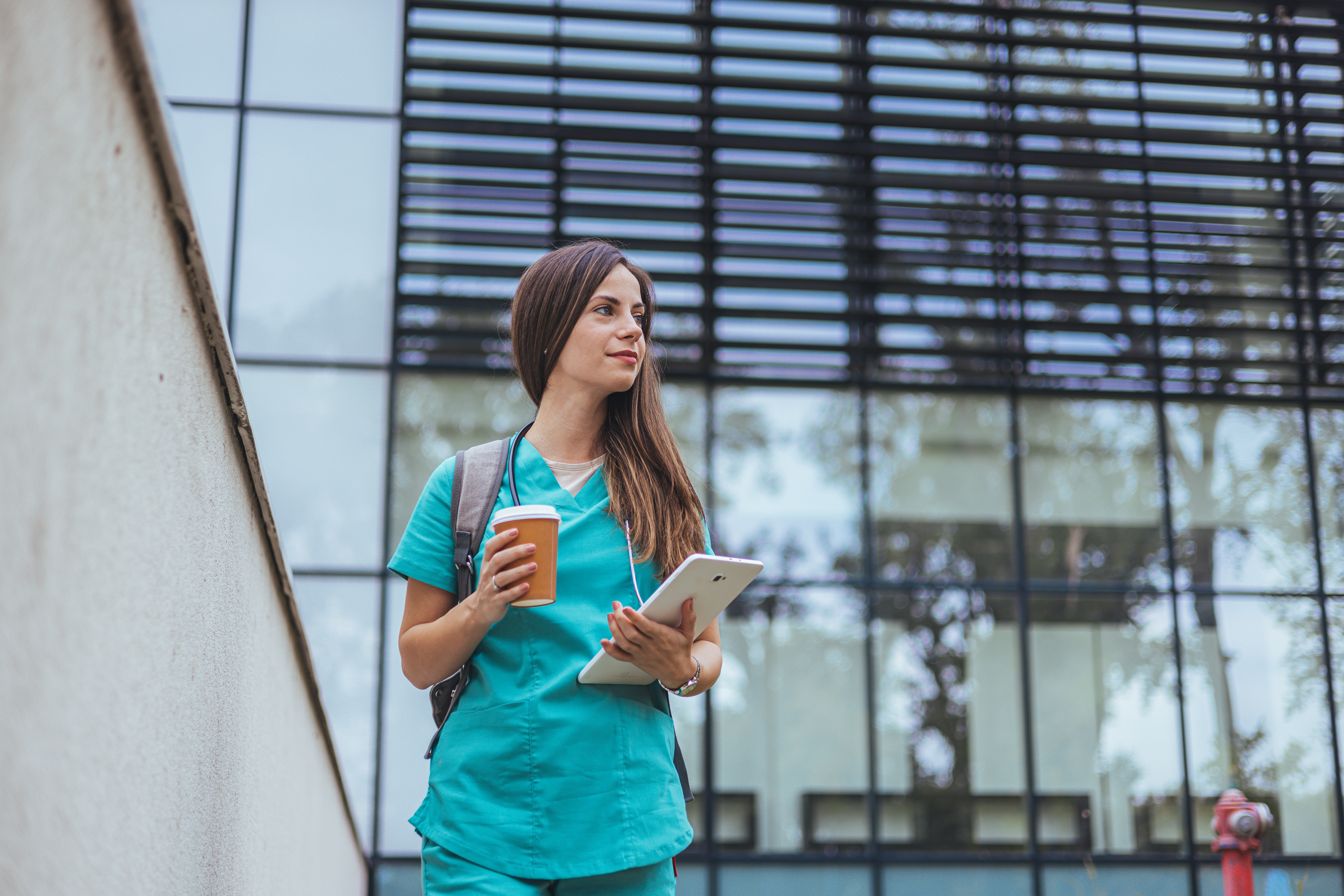 Woman in scrubs standing in front of large glass building